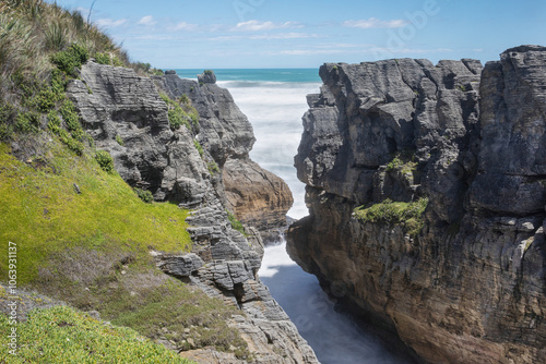 Two steep cliffs with a gap in-between with sea water rushing in.