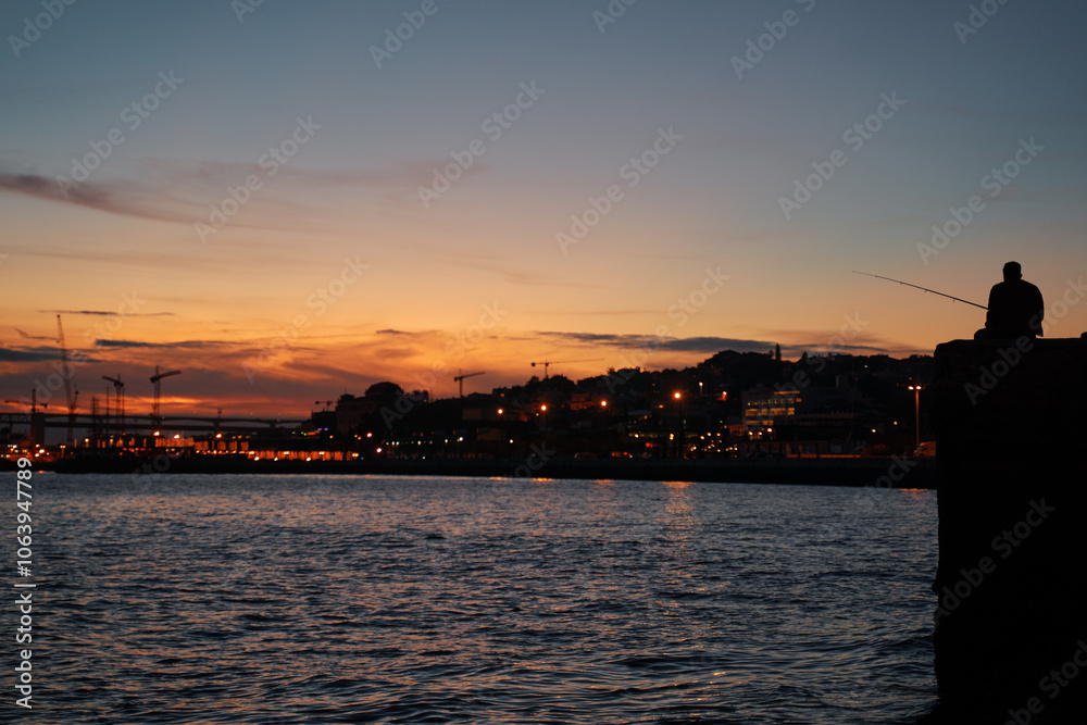 Fototapeta premium Silhouette of people on the Tejo river bank in Lisbon at sunset