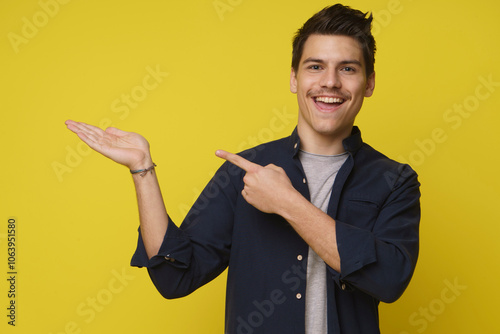 A young man in a blue shirt smiles excitedly, his left hand open and palm up, while his right hand points towards it. A yellow background sets the scene