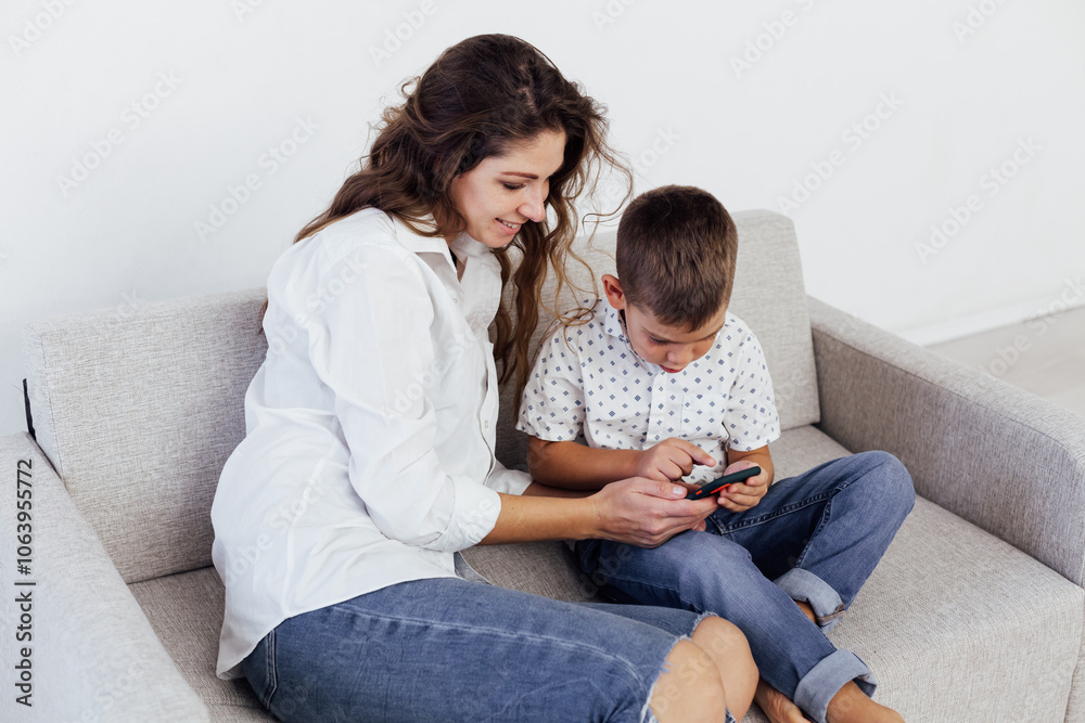 Mom and son sitting home on couch and watching smartphone Mom and son sitting home on couch and watching smartphone