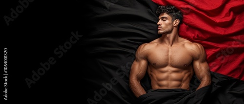 A shirtless man laying in bed under a red and black blanket