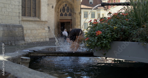 Young boy jumping into outdoor stone fountain splashing water, captured in super slow motion at 800 fps in a public square near historical buildings and flowers