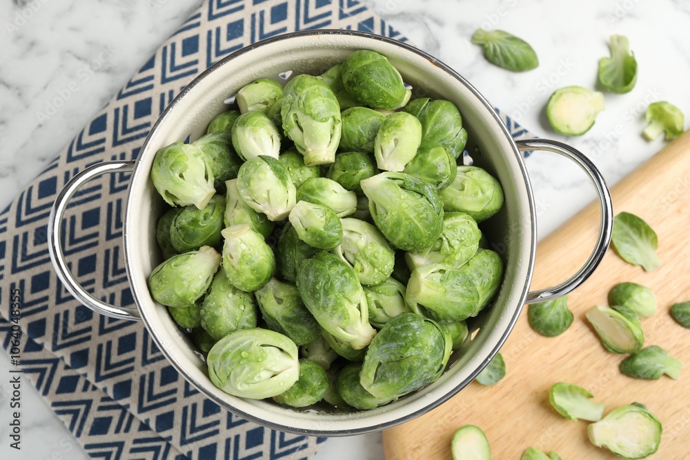 Fresh Brussels sprouts in metal colander on white marble table, top view
