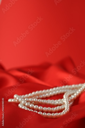 Beautiful pearl necklace on red silk, closeup. Space for text