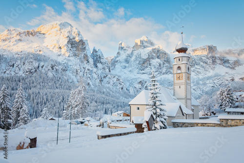 The distinctive church of Colfosco (Kolfuschg) near Corvara with the Sella group Dolomites mountains in the background under a fresh layer of snow in the Alta Badia ski resort in Italy. photo