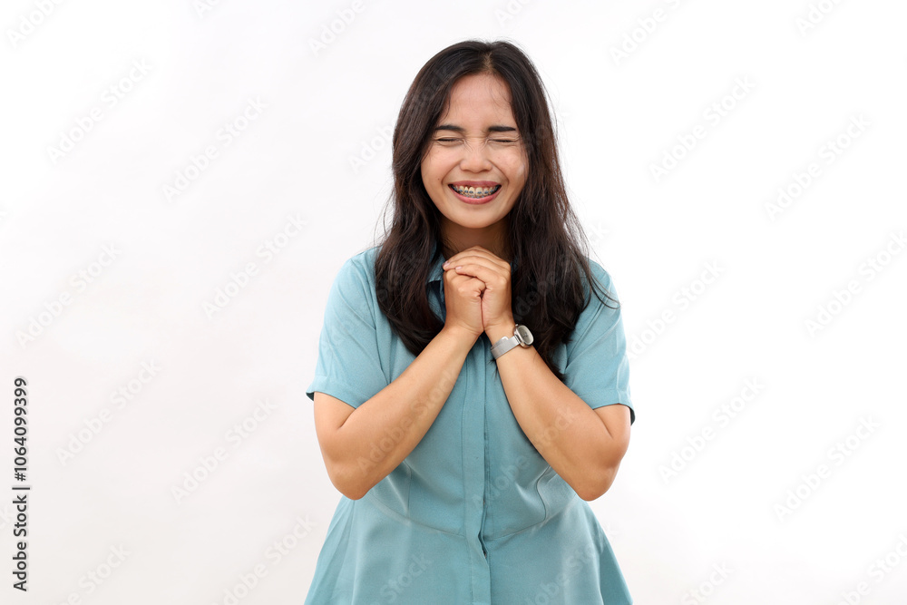 Grateful positive Asian woman clasps hands has beauty face smiles toothily keeps eyes closed dressed in casual casual shirt anticipates something very pleasant isolated over white background Grateful positive Asian woman clasps hands has beauty face smiles toothily keeps eyes closed dressed in casual casual shirt anticipates something very pleasant isolated over white background