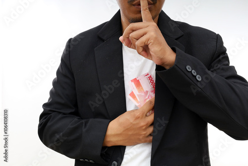 Asian Businessman putting us money into his suit pocket while making silence finger gesture, bribe concept photo