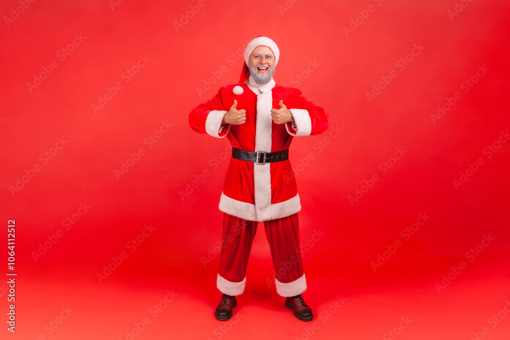 Full length portrait of elderly man with gray beard wearing santa claus costume standing and showing thumb up, approval hand sign, satisfied with result. Full length portrait of elderly man with gray beard wearing santa claus costume standing and showing thumb up, approval hand sign, satisfied with result.