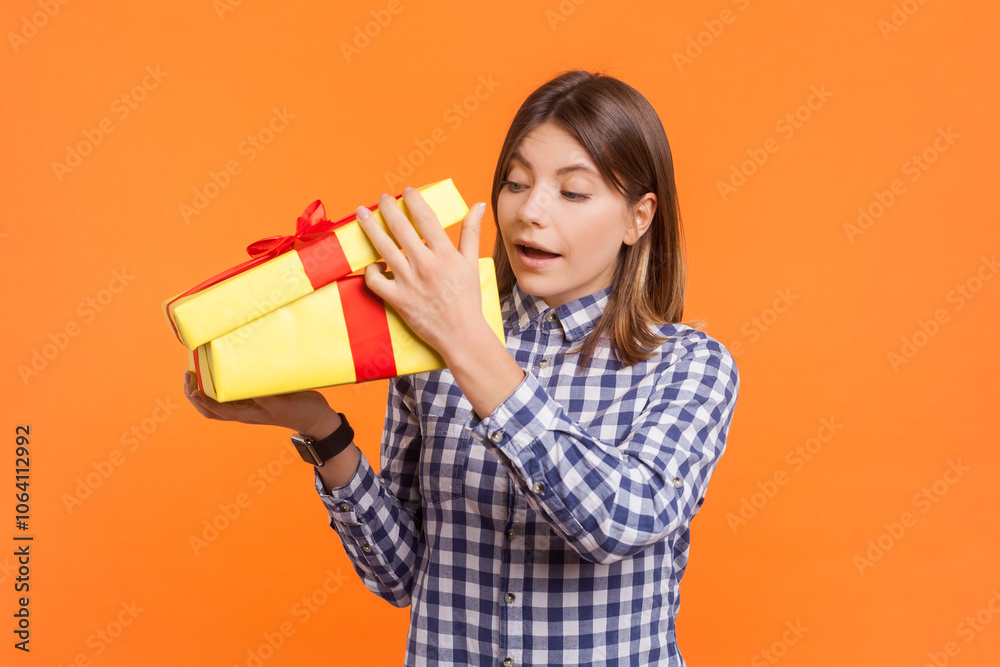 Curious amazed woman with brown hair unpacking yellow wrapped present box watching what inside Curious amazed woman with brown hair unpacking yellow wrapped present box watching what inside