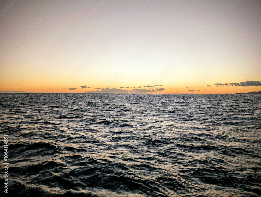 Obraz premium A tranquil sunset over the calm ocean, with gentle waves reflecting warm colors on the water in a serene evening atmosphere