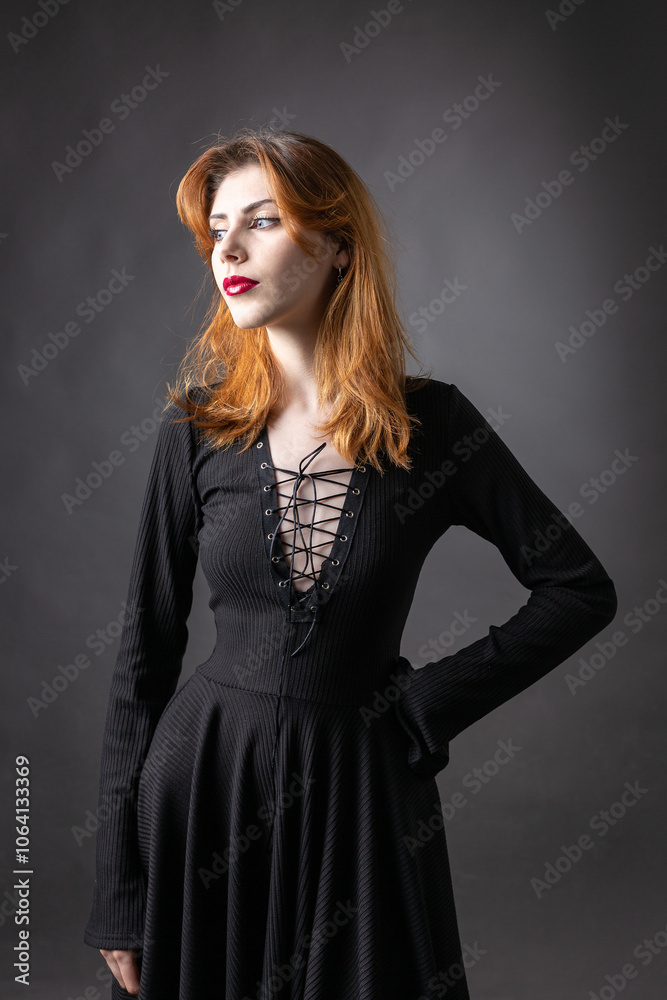 Red-haired gothic girl in a black dress on a gloomy background in the studio. Red-haired gothic girl in a black dress on a gloomy background in the studio.