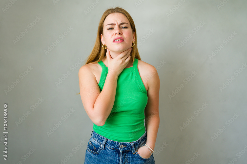 Caucasian woman is standing with a pained expression while touching her neck, suffering from a sore throat Caucasian woman is standing with a pained expression while touching her neck, suffering from a sore throat