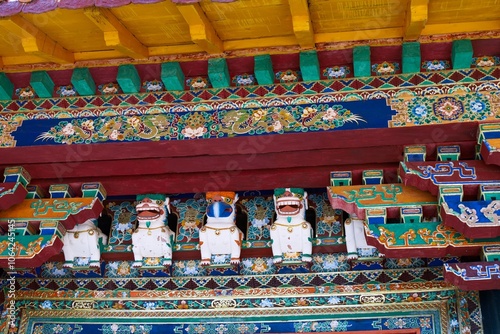 The image showcases the intricate and colorful woodwork of Kalsang Podrang at Norbulingka Palace, Lhasa, Tibet, featuring vibrant Tibetan motifs, guardian figures, and elaborate floral patterns. photo