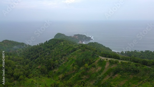 Drone view of Jerit hill Kebumen Indonesia, the seaside with beautiful hills and green trees, coral rocks, waves and ocean