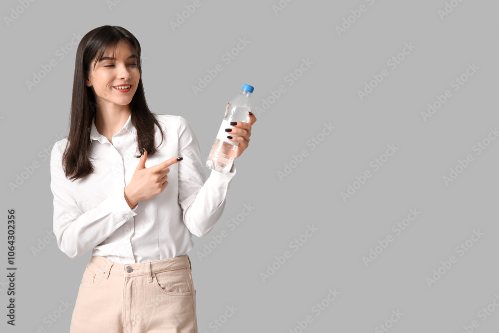 Young Asian woman pointing to bottle of water on grey background Young Asian woman pointing to bottle of water on grey background