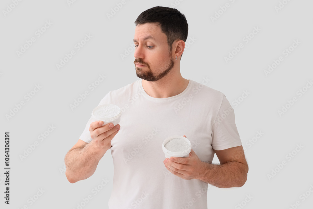 Thoughtful young man with jars of tooth powder on light background Thoughtful young man with jars of tooth powder on light background