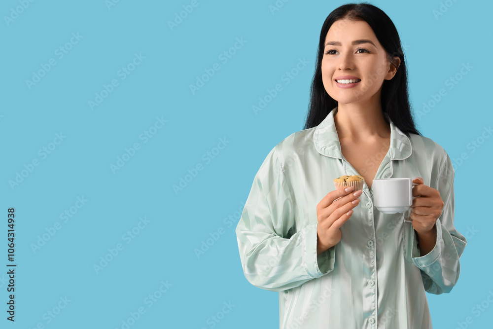 Young woman in pajamas with tasty muffin and cup of coffee on blue background Young woman in pajamas with tasty muffin and cup of coffee on blue background