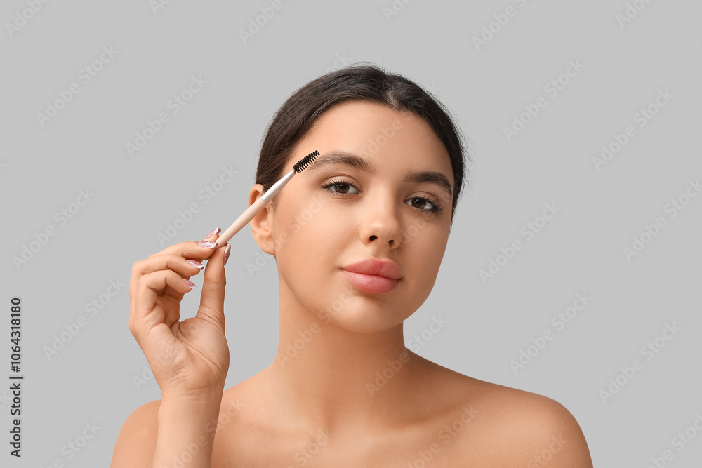 Fototapeta premium Young woman correcting shape of her eyebrows on grey background