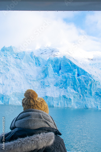 WOMAN WITH YELLOW BEANIE LOOKING AT A HUGE ICEBERG IN ARGENTINA PATAGONIA photo