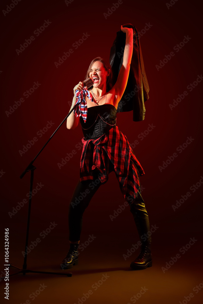 Fototapeta premium Beautiful female singer with microphone on dark red background