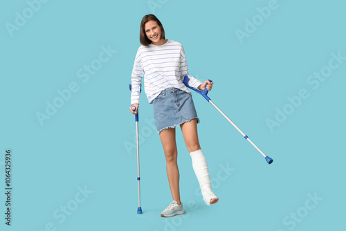 Young woman with broken leg and crutches on blue background