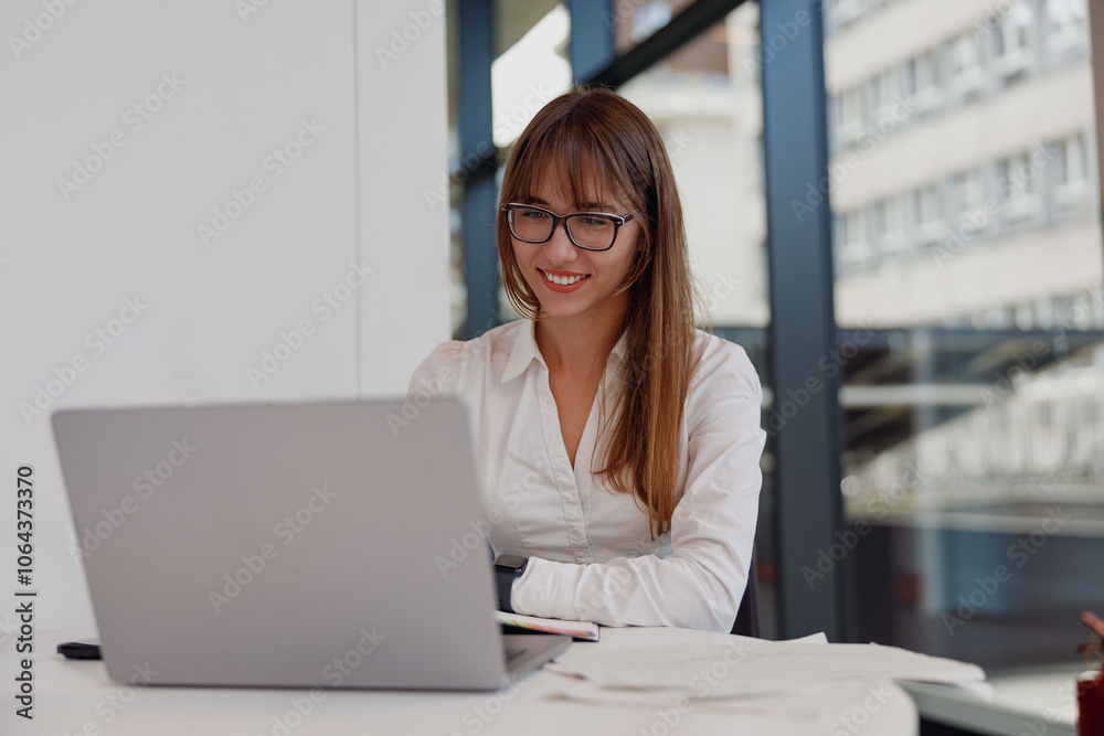 A professional woman smiles while using her laptop in a bright office, embodying productivity and focus. A professional woman smiles while using her laptop in a bright office, embodying productivity and focus.