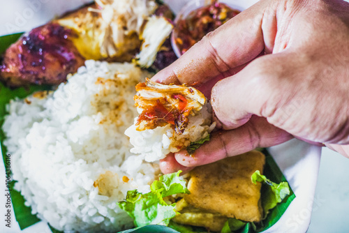 People enjoy grilled chicken rice with spicy chili sauce and vegetables using their hands or Fingerfood or muluk. A noble tradition of Javanese culture photo