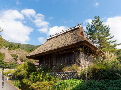 茅葺き屋根の農機具小屋と秋の風景