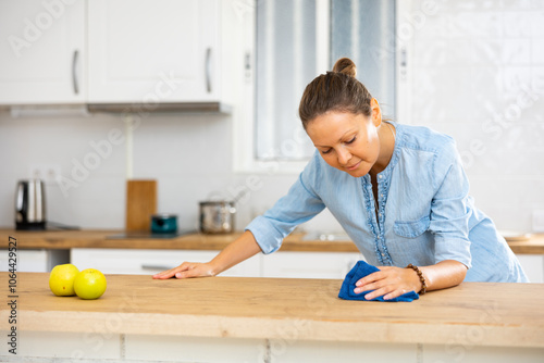 Cheerful young woman wiping dust from kitchen surfaces, everyday household chores concept