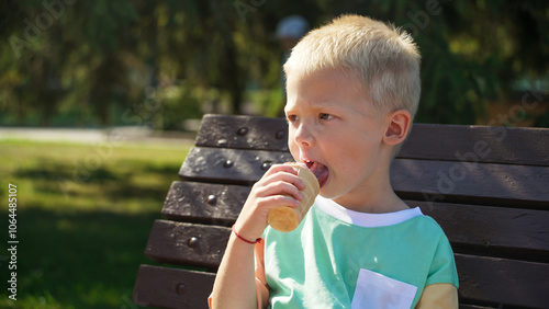 A young boy sits on a bench, savoring an ice cream cone with a look of delight. The sun shines brightly, creating a cheerful atmosphere in the park.