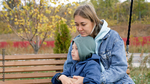 A mother and son share a tender moment while sitting on a park bench, enjoying each other's company and the beautiful surroundings during their family weekend together.