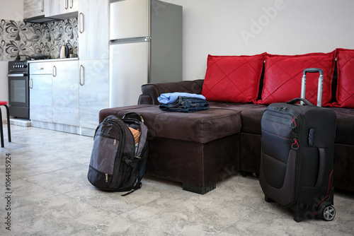 Modern suitcase on wheels and backpack in the living room near the sofa and kitchen. photo