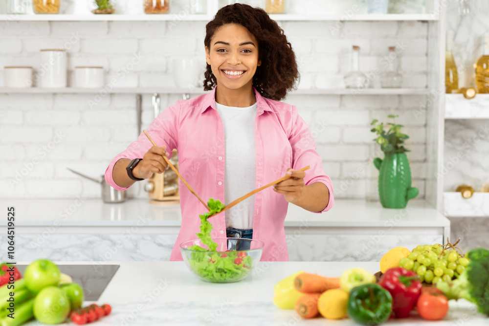 Dieting Concept. Smiling black girl cooking and mixing fresh vegetable salad in glass bowl, copy space Dieting Concept. Smiling black girl cooking and mixing fresh vegetable salad in glass bowl, copy space