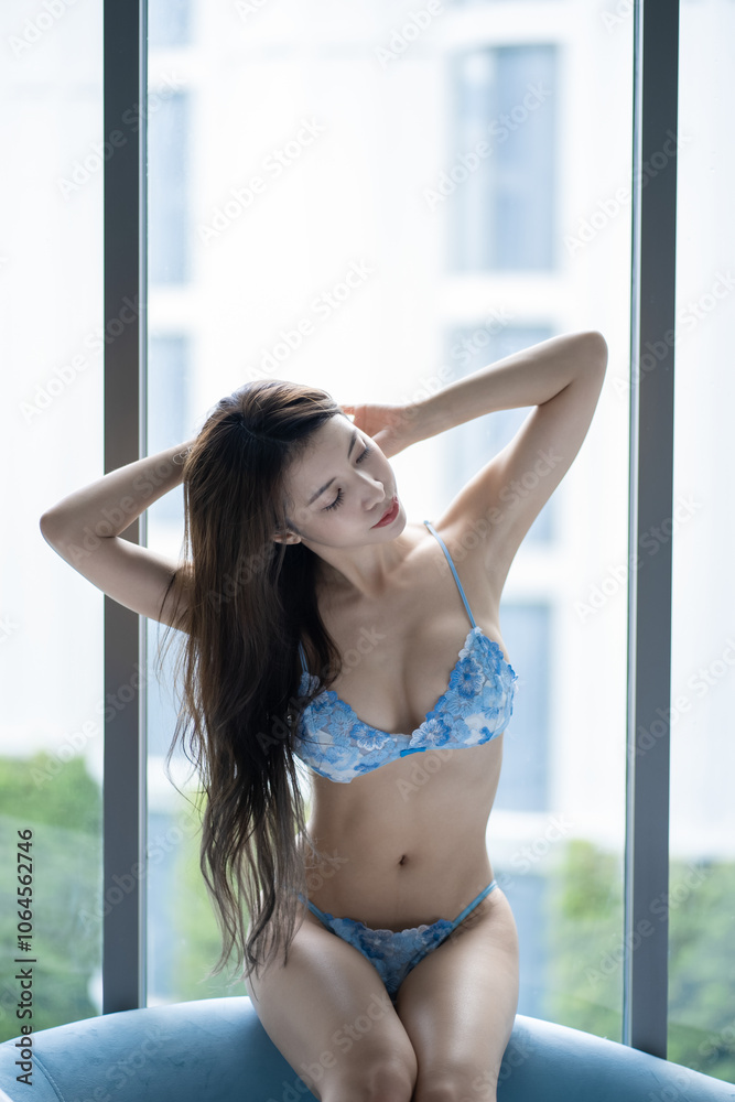 Woman in blue sexy bikini posing by the window with daylight. Woman in blue sexy bikini posing by the window with daylight.