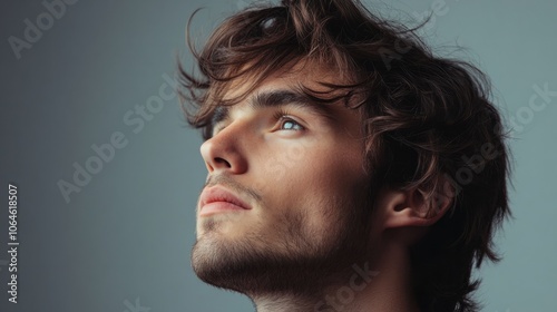 Man with thick, wavy hair gazing thoughtfully into the distance on a plain gray background