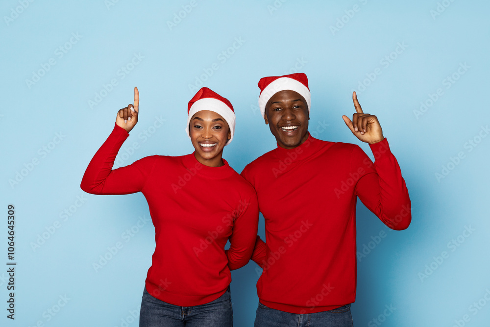 A cheerful couple dressed in matching red sweaters and Santa hats poses with raised hands, smiling brightly against a light blue background, embodying the spirit of the holiday season. A cheerful couple dressed in matching red sweaters and Santa hats poses with raised hands, smiling brightly against a light blue background, embodying the spirit of the holiday season.