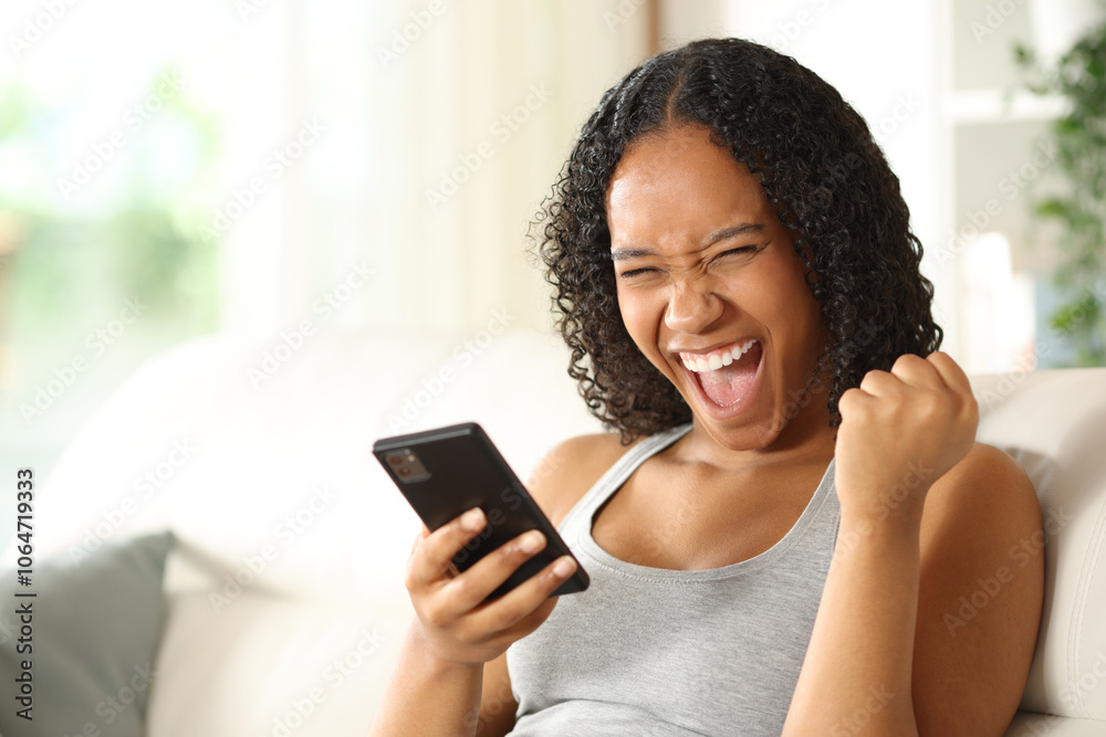 Excited woman holding phone celebrating at home