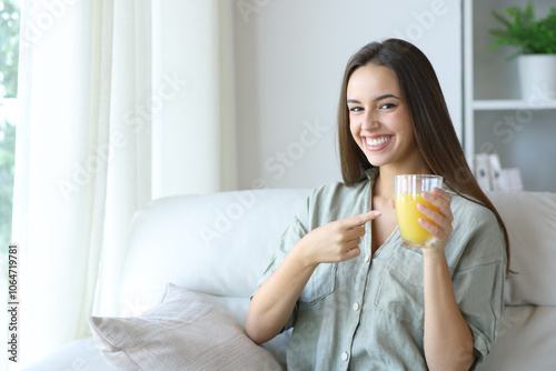 Happy woman at home showing glass with orange juice