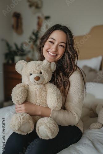 A woman is sitting on a bed holding a teddy bear. She is smiling and she is happy photo