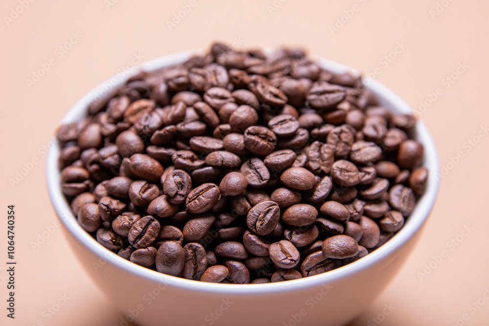 Roasted coffee beans in white ceramic bowl isolated on brown background Roasted coffee beans in white ceramic bowl isolated on brown background