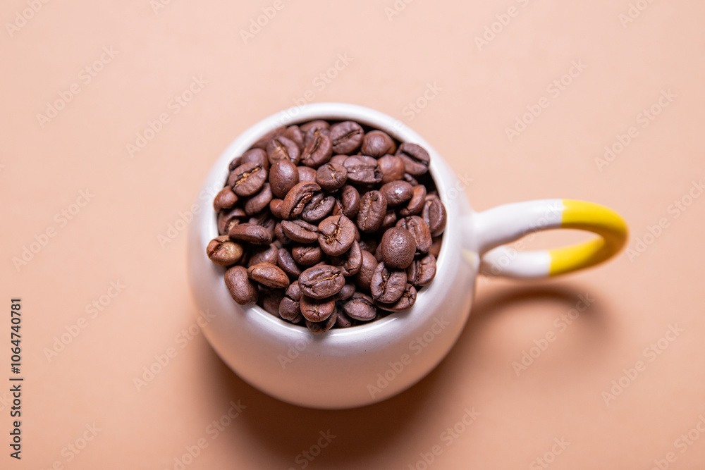 Small roasted coffee beans in white ceramic mug isolated on brown background Small roasted coffee beans in white ceramic mug isolated on brown background