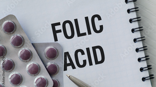 A bottle of pills and a pen on a notebook with the word Folic Acid written on the notebook photo