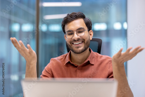 Business man smiling during video call from office. He exudes positivity and communication. Ideal for concepts of remote work, virtual meetings, and professional interaction.