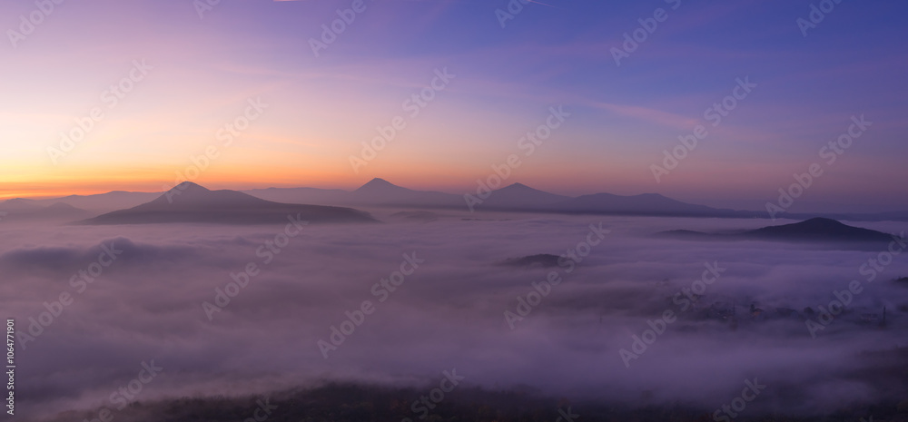 Obraz premium Hills in foggy evening. Radobyl hill in Czech Midland/ Ceske Stredohori, Czech republic