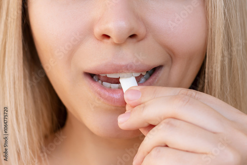 Cropped shot of a young caucasian blonde woman holding chewing gum in the hand putting it in her mouth. Mint bubble gum for fresh breath