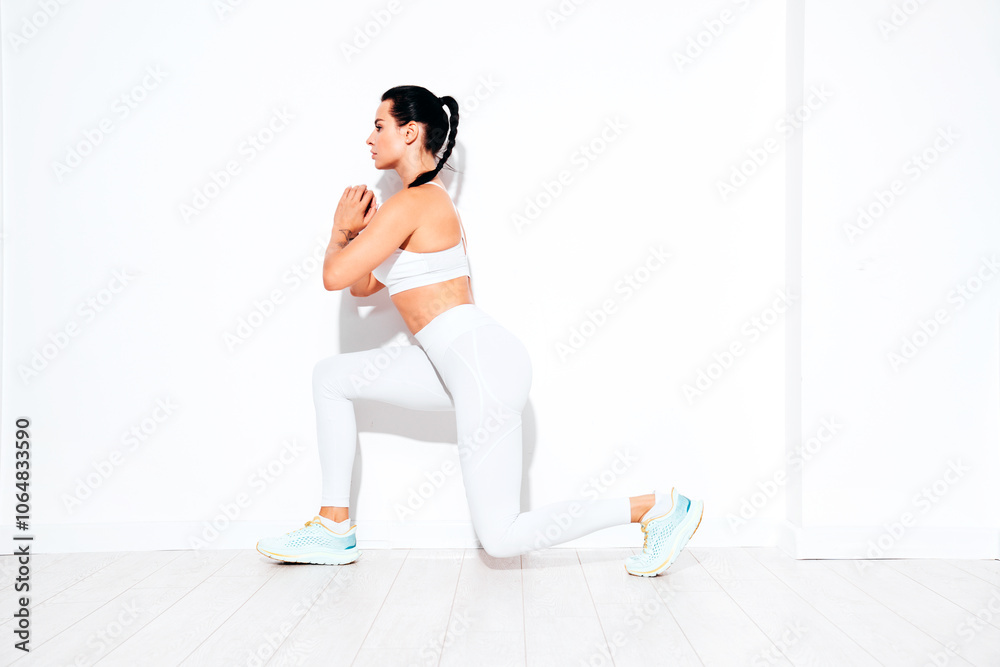 Fototapeta premium Fitness confident woman in white sports clothing. Sexy young beautiful model with perfect body. Female isolated on white wall in studio. Stretching out before training, makes lunges