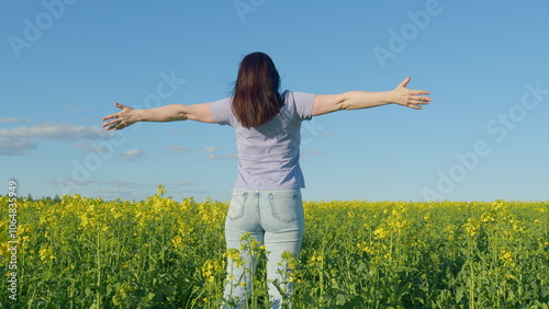 Woman In A T-Shirt Standing In A Flowering Canola Rapeseed Field. Pretty Young Woman With Arms Raised In Air In Rapeseed Field.