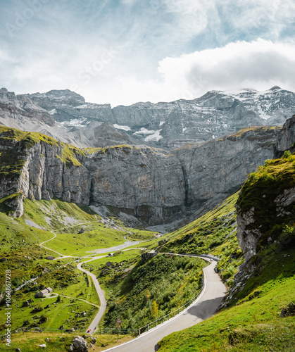 Winding road in Swiss alps. Curvy road near cliff rock in Urner Boden valley, snow-capped mountain peaks in the background. Klausen Pass - mountain pass in Glarus Alps.  photo