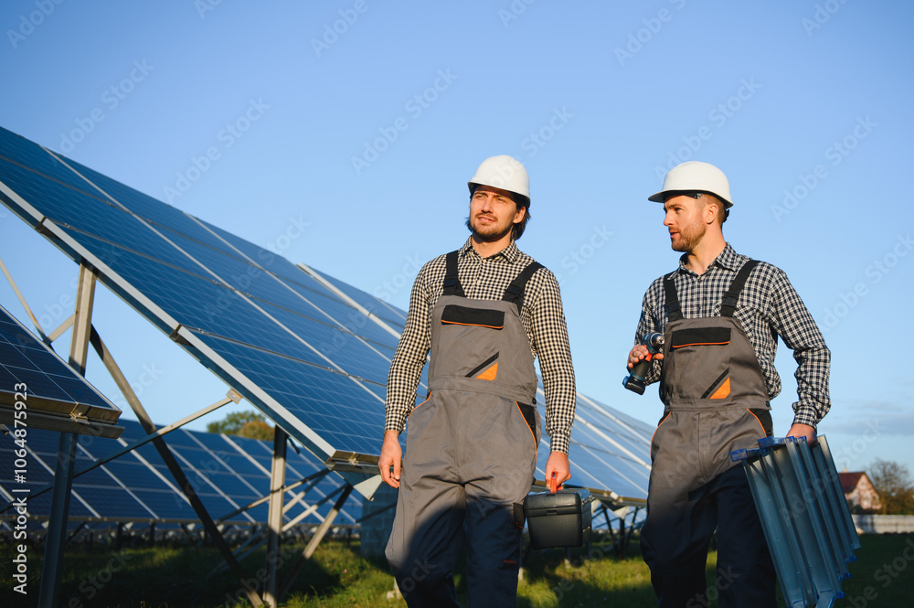 Two skilled workers or craftsmen wearing working gray uniforms, technicians are installing solar panels on a solar farm for clean energy and electricity supply Two skilled workers or craftsmen wearing working gray uniforms, technicians are installing solar panels on a solar farm for clean energy and electricity supply