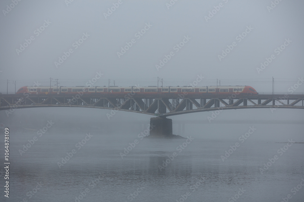 The SKM (Fast Urban Railway) train crossing the Vistula River on the Średnicowy rail bridge in Warsaw on a magically foggy October day. The SKM (Fast Urban Railway) train crossing the Vistula River on the Średnicowy rail bridge in Warsaw on a magically foggy October day.